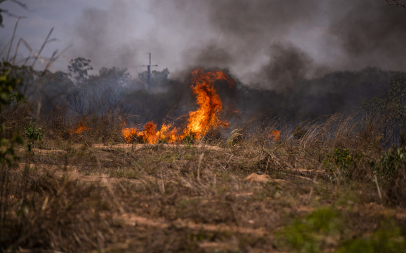 Fire with billowing black smoke in a dry, brown and burning landscape.