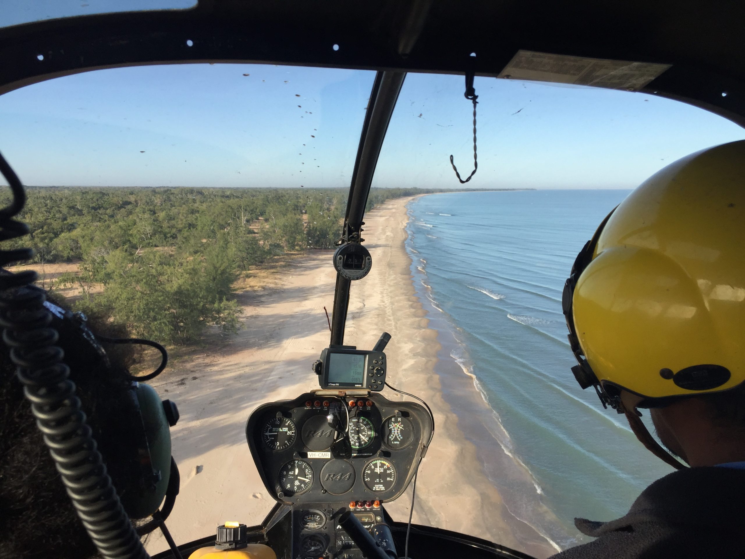 Photo of a view through the front window of a helicopter conducting a survey flight over a Cape York coastline.