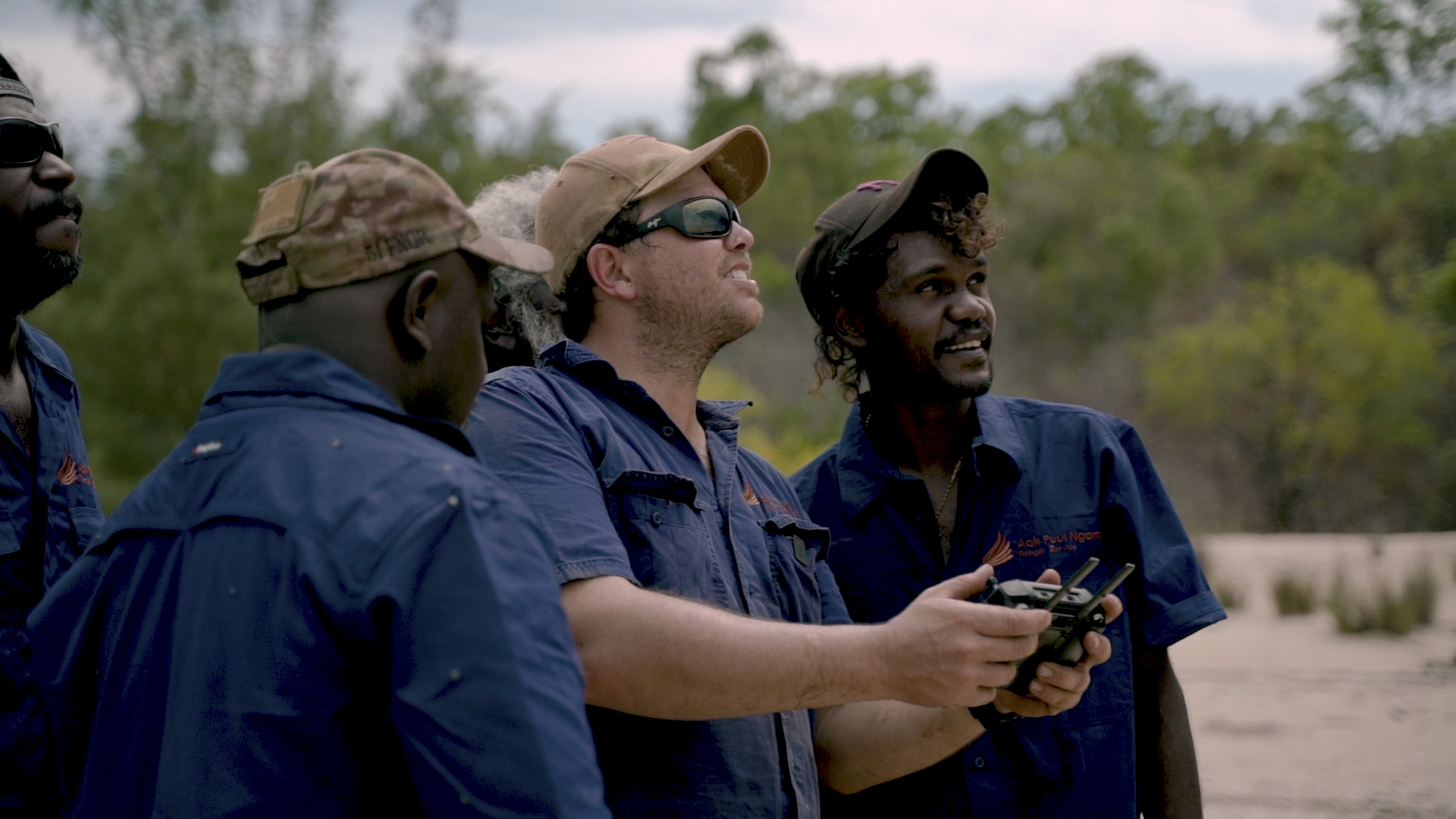 A group of APN rangers gather around one ranger flying a drone.