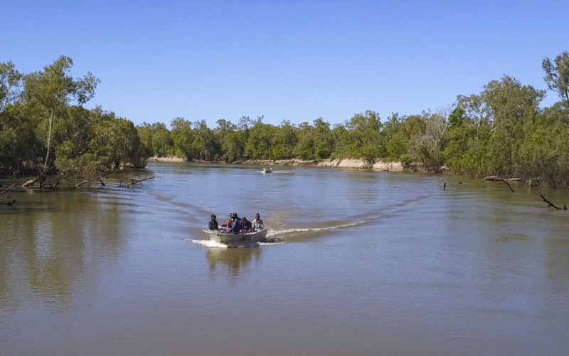 Aerial image of rangers in a tinny travelling down a Cape York river with trees, mangroves and sandy banks visible.