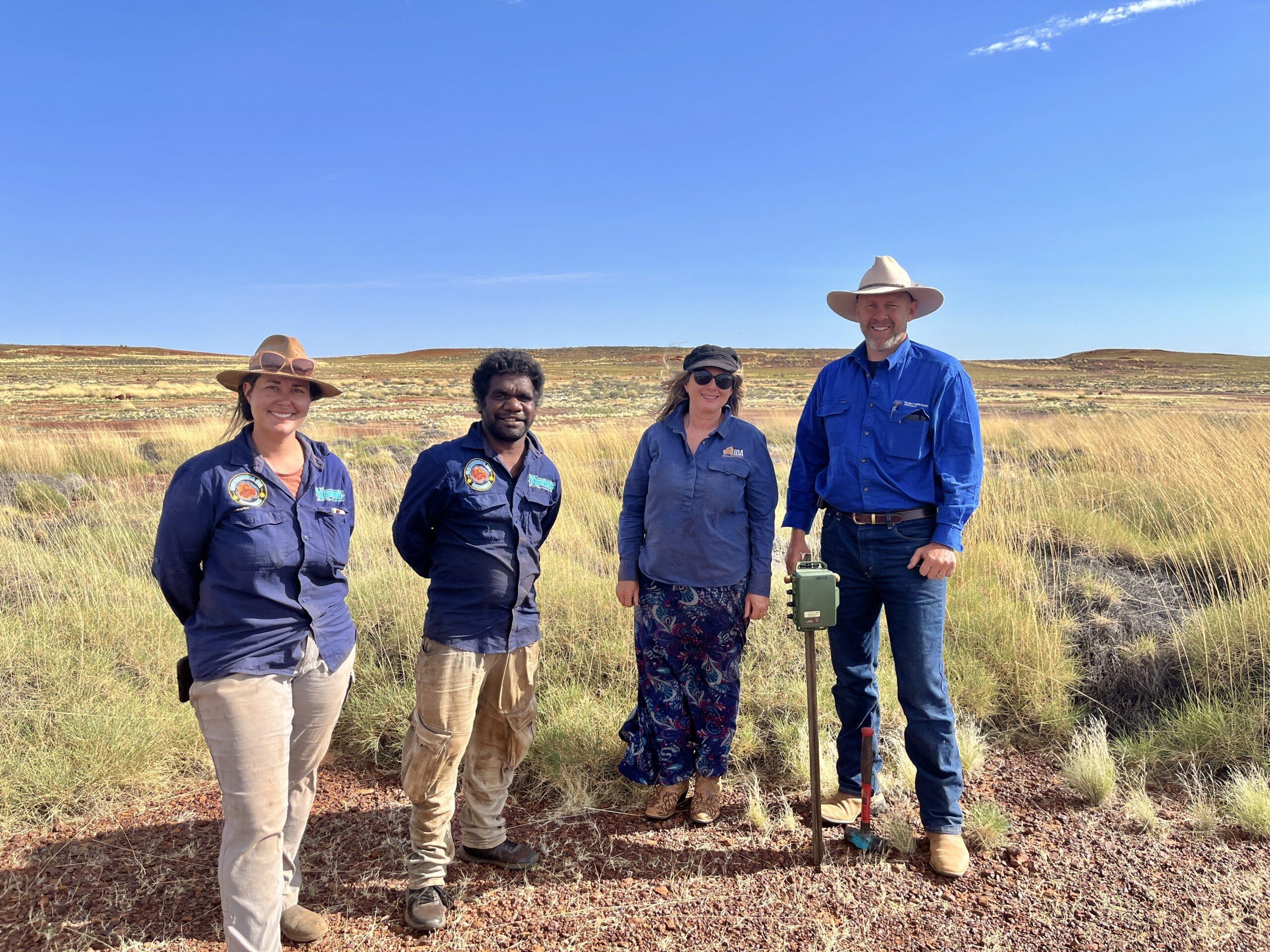 Four people stand smiling at the camera in a desert